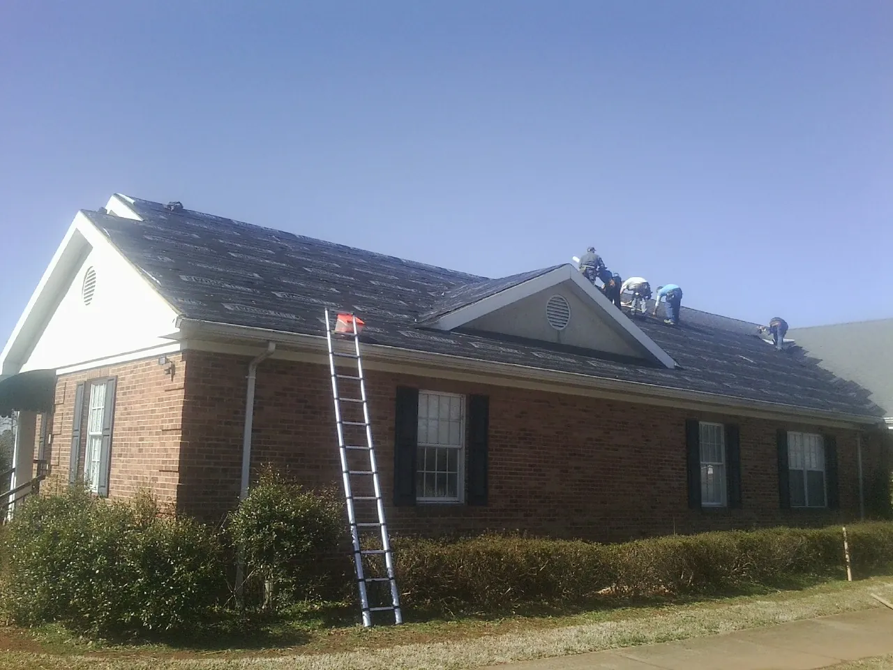 Crew tearing shingles off a brick ranch roof with a ladder set — Emergency Roof Repair work by our crew in Oconomowoc