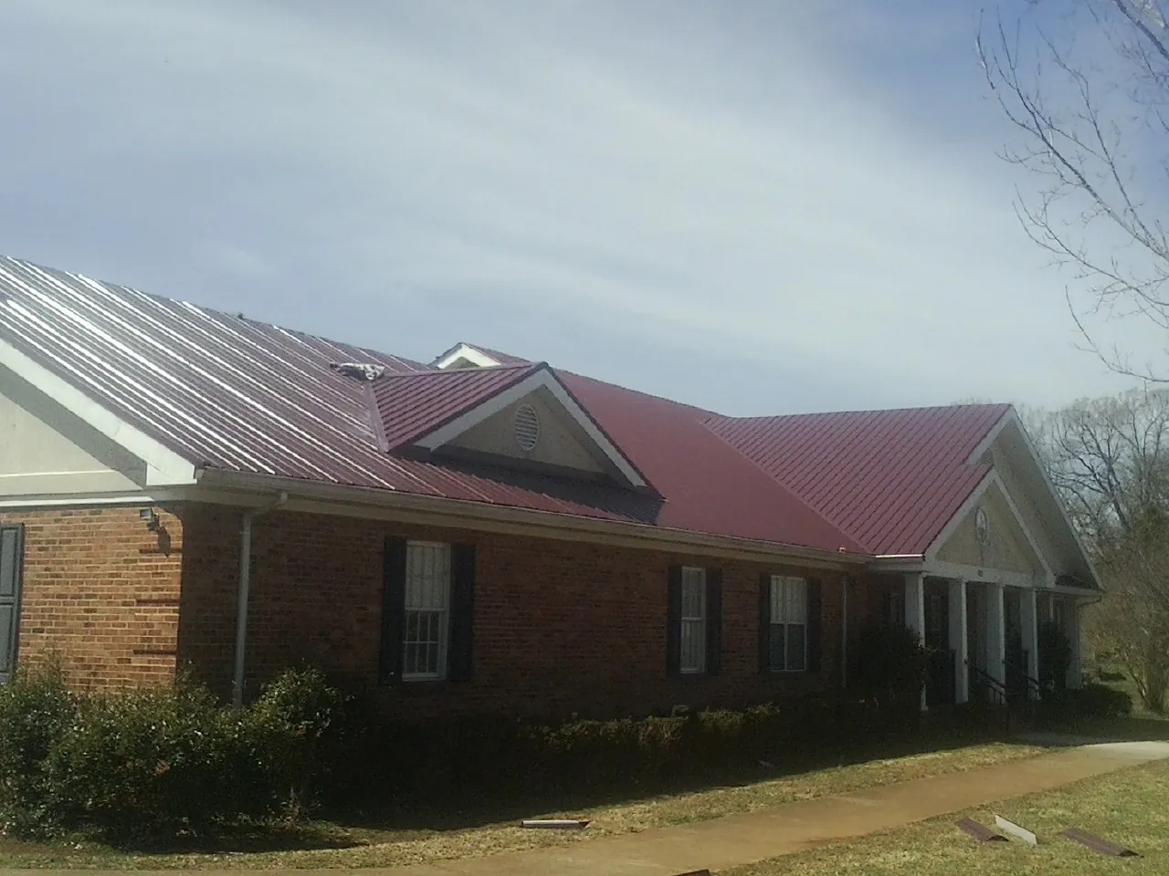 Red metal roof with gabled entries on a long brick building, from a Hail Damage Roof Repair job in Oconomowoc