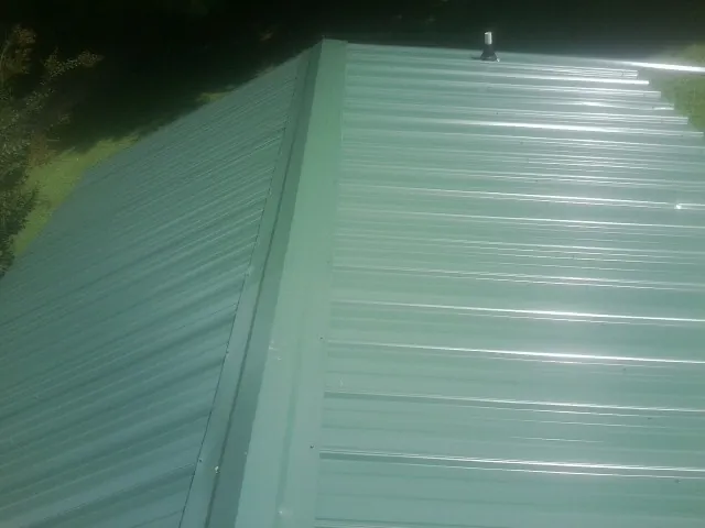 New green metal panels meeting at the ridge of a roof — Flat Roof Repair work by our crew in Oconomowoc