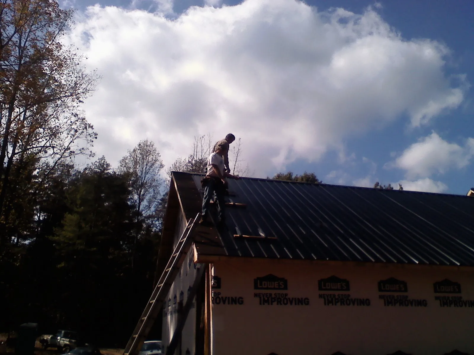 Roofer fastening dark metal panels high against a cloudy sky, from a Roof Inspection job in Oconomowoc
